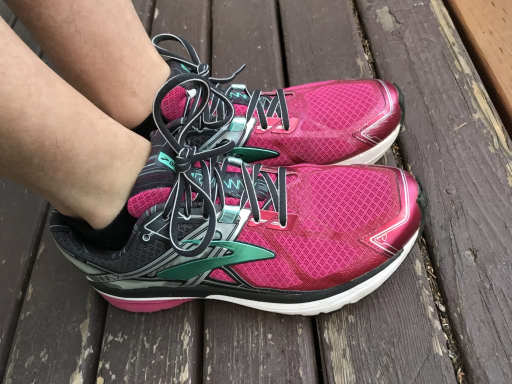 A pair feet wearing hot pink running shoes on a wooden floor.