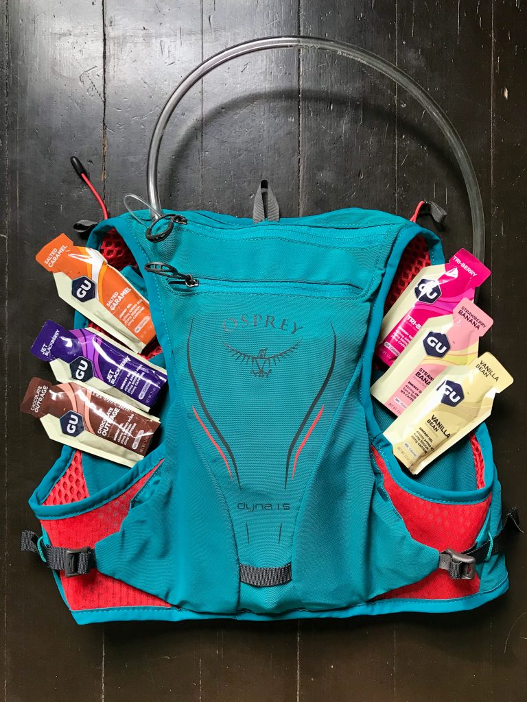 A teal hydration pack with 6 Gu energy gels on either side of the pack.