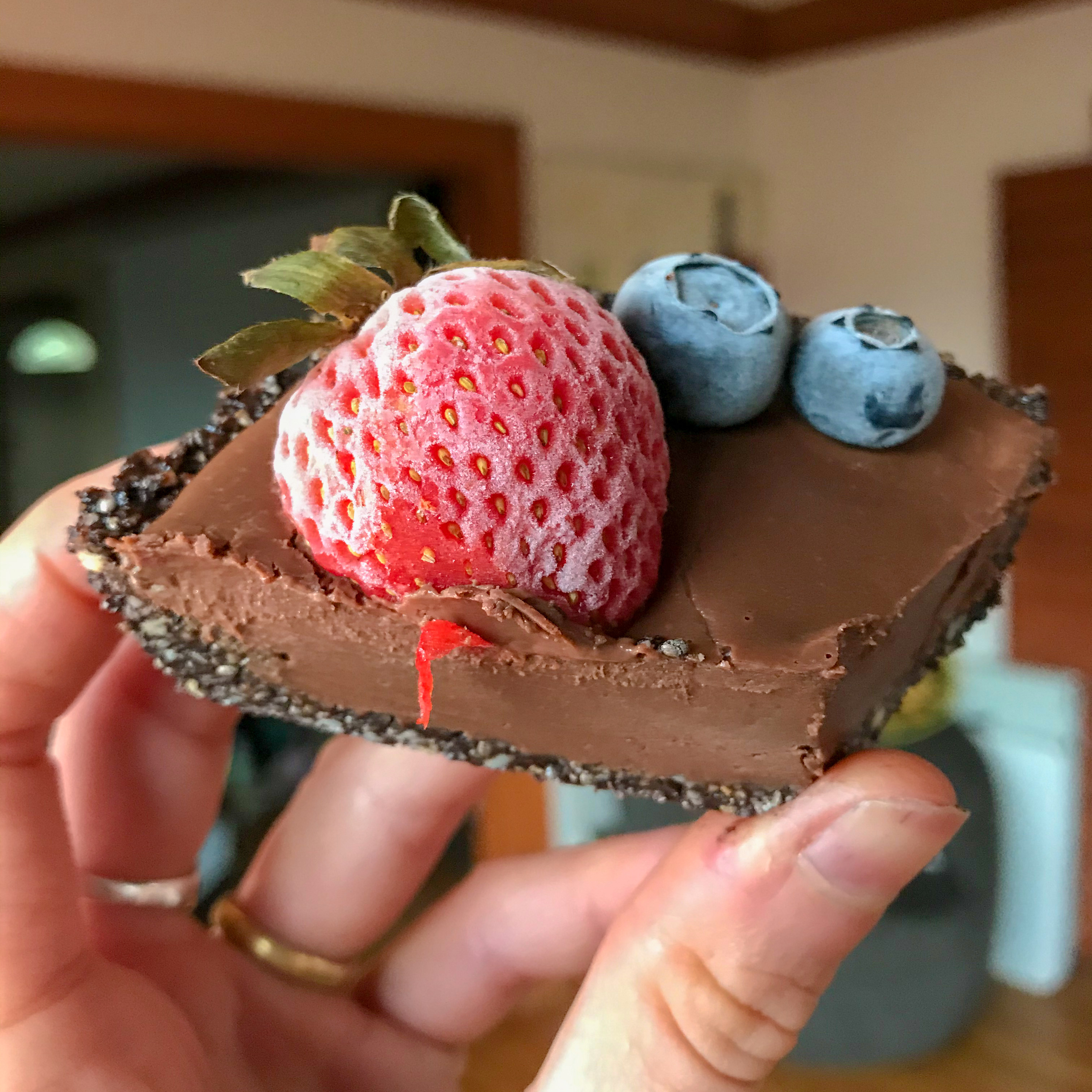 A slice of the vegan chocolate tarte with a frozen strawberry and 2 blueberries on top.