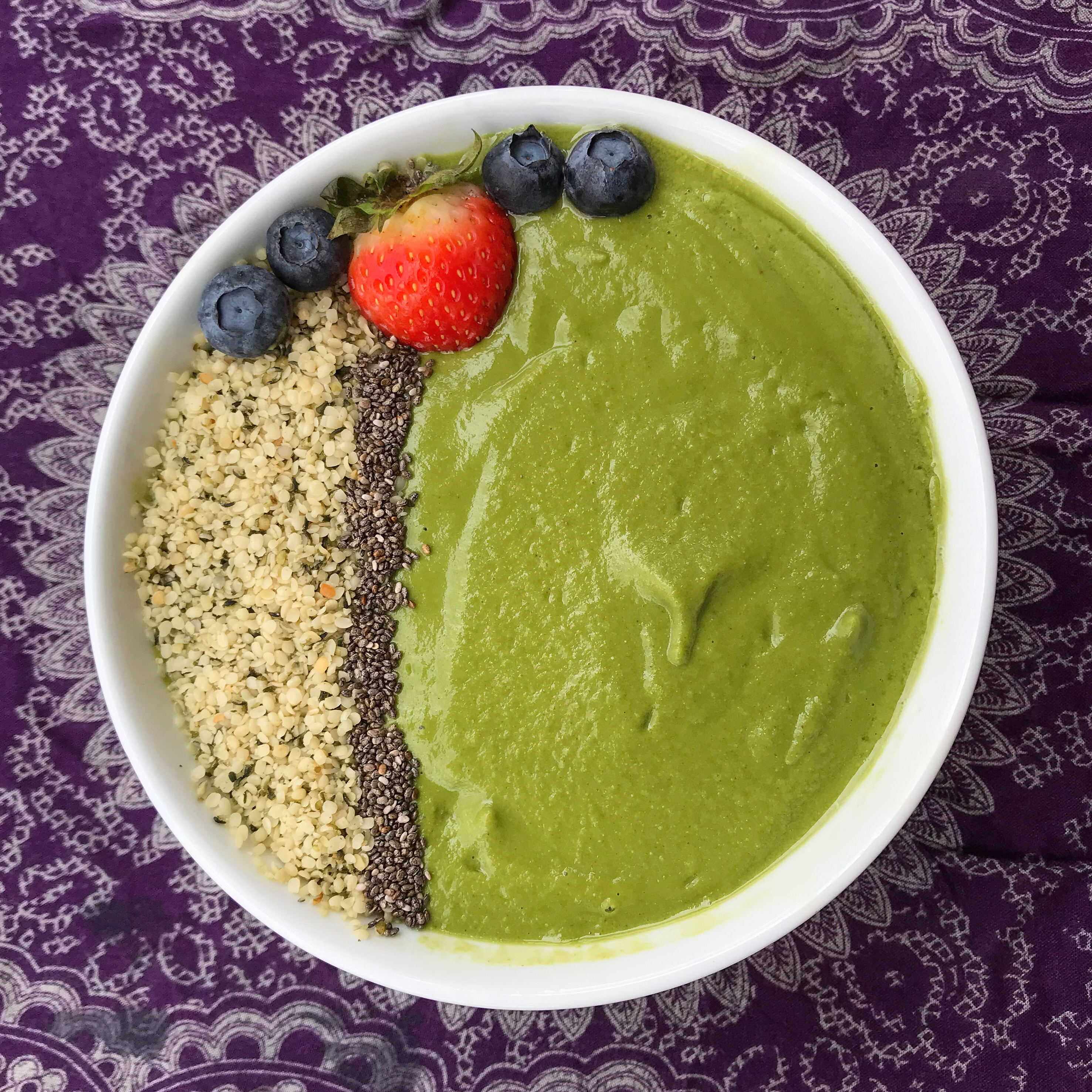 A green smoothie with arranged hemp and chia seeds, plus a strawberry and 4 blueberries as garnish.