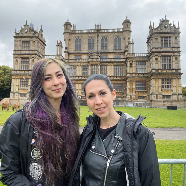 Ronnie and Catherine, two vegan goth friends, stand in front of the neo-Gothic Wollaton Hall under an overcast sky.