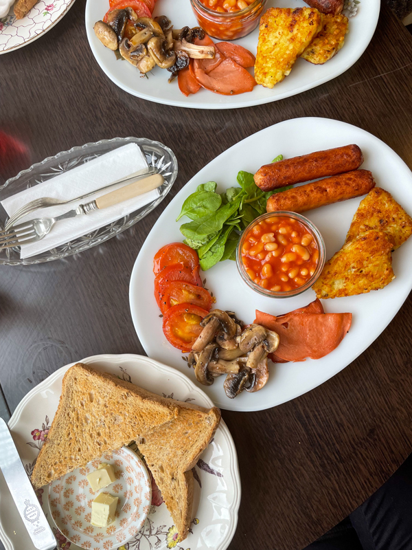 A full English breakfast consists of vegan sausage, sweet baked beans, hash browns, toast, fresh spinach, and grilled mushrooms and tomatoes.