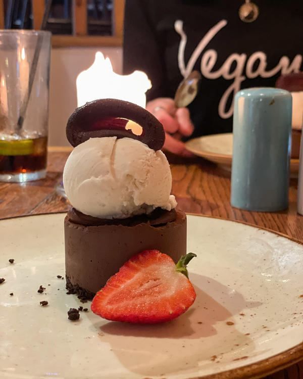 A cylindrical chocolate torte with a scoop of vanilla bean ice cream and a piece of chocolate on top, plus a strawberry half on the side.