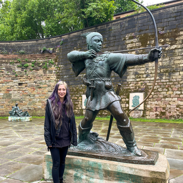 Ronnie stands next to the bronze Robin Hood Statue in front of the stone wall of Nottingham Castle.