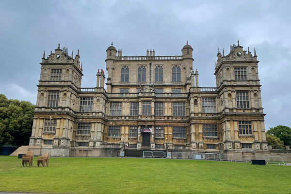 The grand neo-Gothic Wollaton Hall features dark pointed arched windows and spires under a cloudy sky.