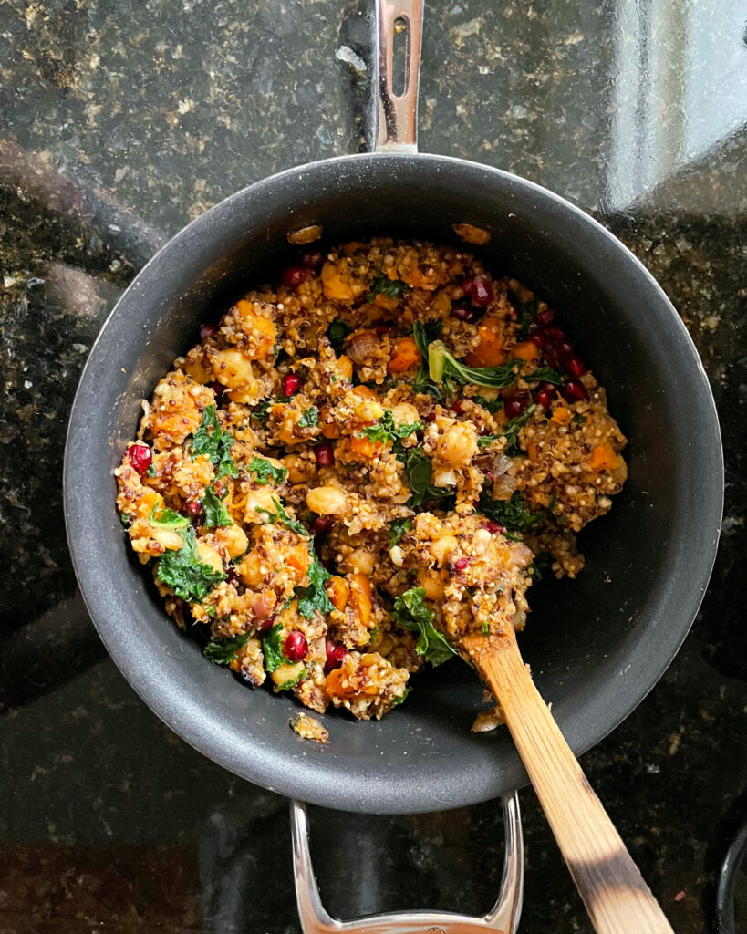 The colorful quinoa stuffing in a pot with a wooden spoon sticking out.