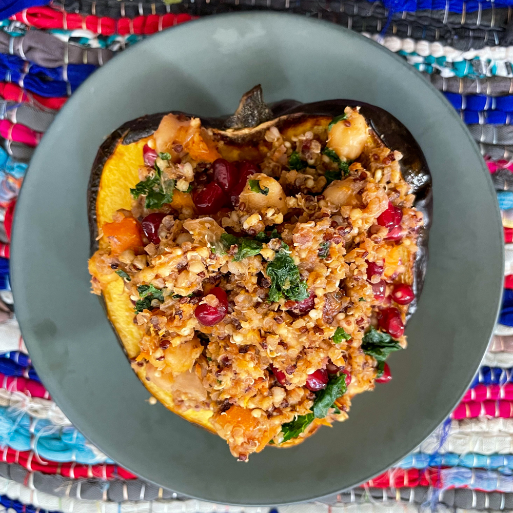 Stuffed acorn squash with quinoa stuffing on top of a gray plate against a colorful woven rug.