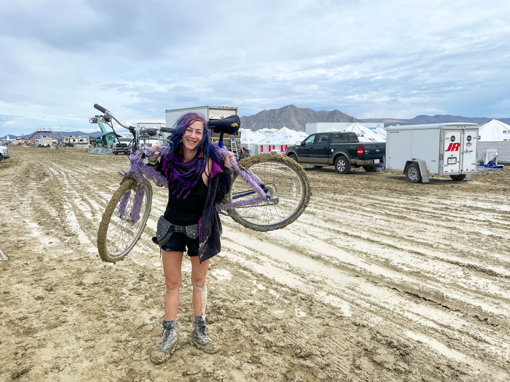Ronnie carries her bike in the playa mud.